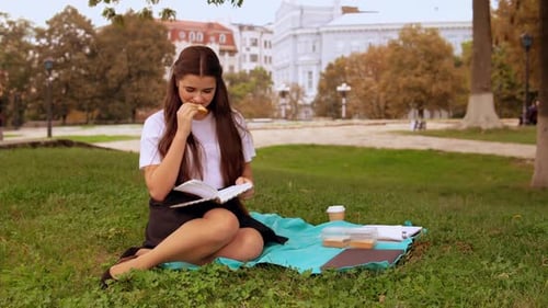 Woman Reads Book in Grassy Urban Park