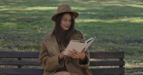 Woman Reads Book on Park Bench on Sunny Day