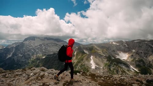Seitenansicht einer wandernden Touristin, erobert und bestiegen Gipfel in orangefarbener Jacke und Rucksack