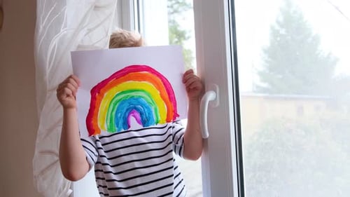 Blond Boy Smiles Holding Rainbow Drawing