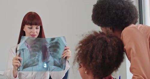 Doctor Reviews X-Ray with Woman and Child