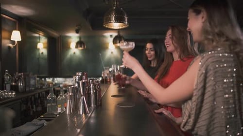 Trois femmes heureuses cliquettent des verres assis au comptoir du bar