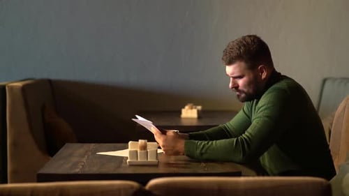 Junger attraktiver bärtiger Hipster-Mann sitzt im Café und liest Papierdokumente