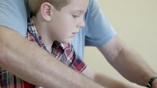 Grandfather helping his grandson cut a piece of wood in a band saw.