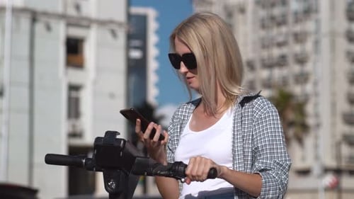 Woman Using Phone With Electric Scooter in City
