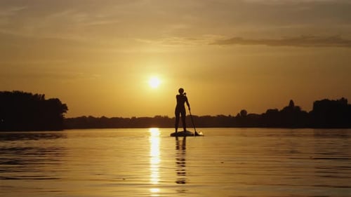 Paddleboarder Silhouette Glides Across Golden Sunset Waters