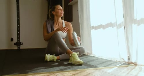 Fit tired woman refreshing with bottle of water in fitness club