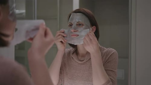 Woman Applies Gray Sheet Mask in Bathroom
