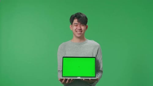 A Smiling Asian Man Holding Green Screen Computer While Standing In Front Of Green Screen Background