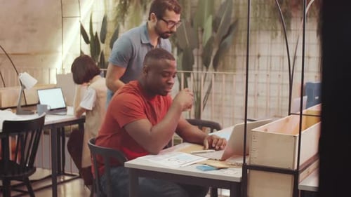 Divers hommes travaillant avec des documents et utilisant un ordinateur portable dans le cadre du coworking