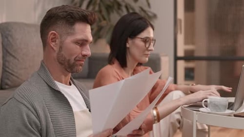 Woman Using Laptop and Man Reading Documents