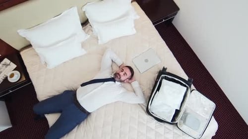 Relaxing Businessman Lays on Bed in Hotel Room
