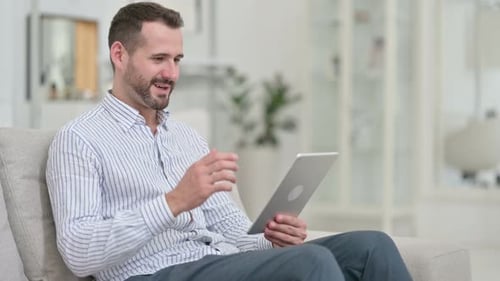 Man Celebrates Using Tablet on Couch Indoors