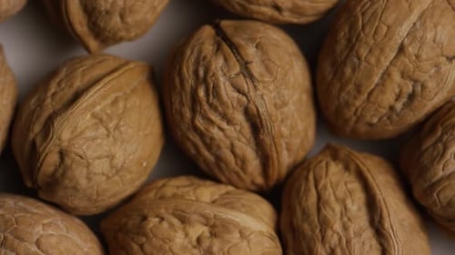 Cinematic, rotating shot of walnuts in their shells on a white surface - WALNUTS