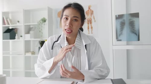 Young Asian lady doctor using computer laptop talking video call with patient in hospital