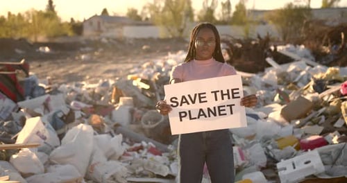 Young Adult Holding 'Save the Planet' Sign at Landfill