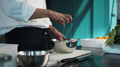 Professional restaurant kitchen: chef breaks eggs in a bowl