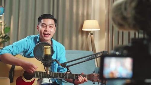 Hombre asiático tocando la guitarra y cantando una canción. El hombre está transmitiendo para su canal de redes sociales