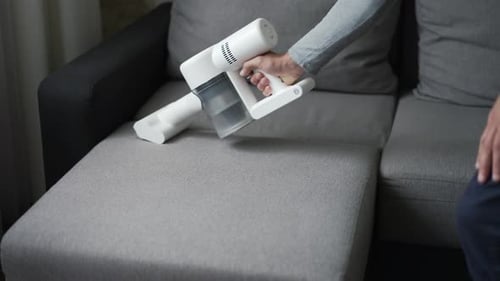 Man Vacuuming Gray Couch with Cordless Vacuum Cleaner