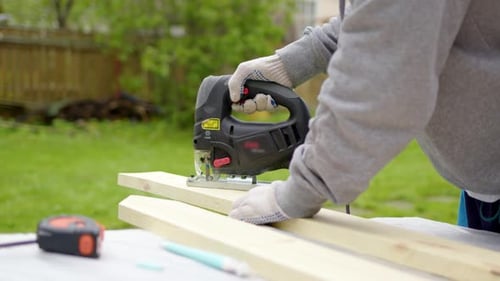 Unrecognizable Worker in Nature Sawing Board with Electric Jigsaw