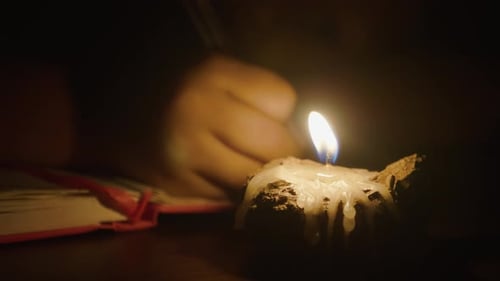 Nahaufnahme von Kind Mädchen schreibt mit Stift in Kerzenlicht im dunklen Raum