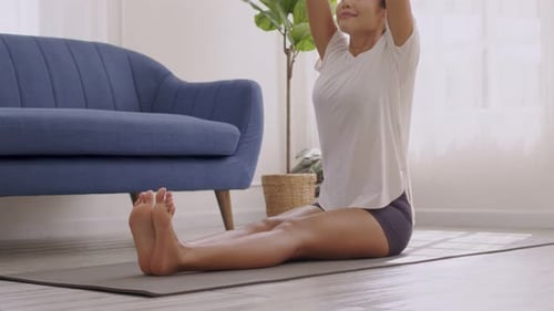 In the morning, an Asian woman is doing yoga, sitting forward bend exercise