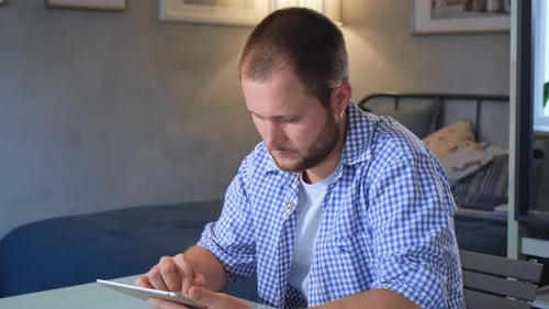 Man at home working on digital tablet. Close-up of young Caucasian guy use tablet