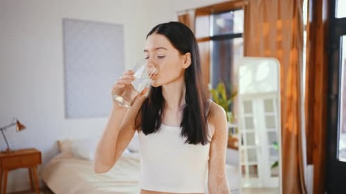Woman Takes Pill and Drinks Water in Bedroom