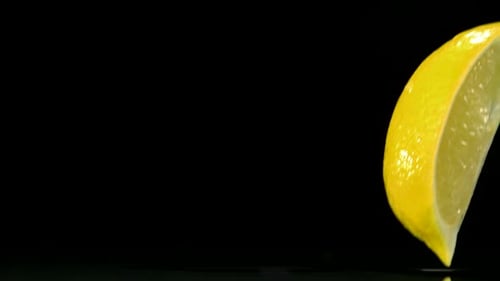 Slo-motion lemon falling into wedges against black drop