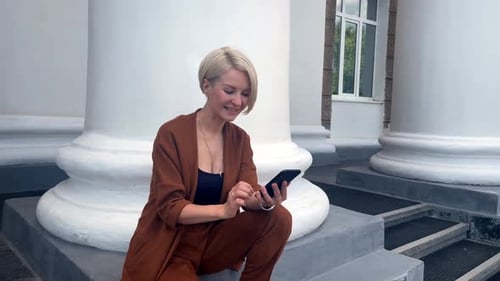 Woman Celebrates Success on Phone Sitting on Steps