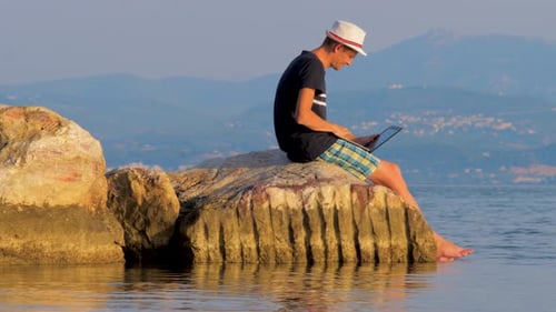 Adult Working on Laptop Sitting on Rocks by Lake