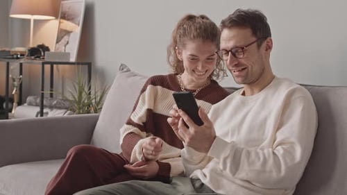 Smiling Couple Using Smartphone on Couch Together