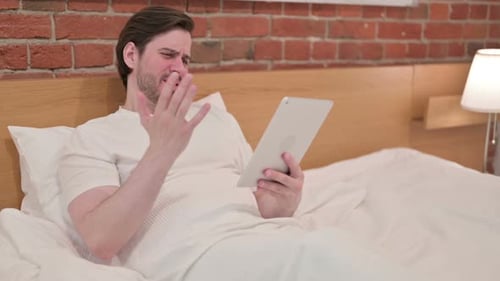 Man Lying in Bed Using Tablet, Experiencing Frustration