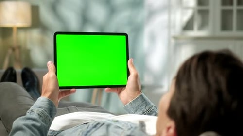 View From the Shoulder of Man Using Hand Gestures on Green Mock-up Screen Digital Tablet Computer in