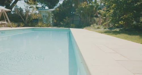 Tracking shot of a swimming pool in a large back yard of a large house