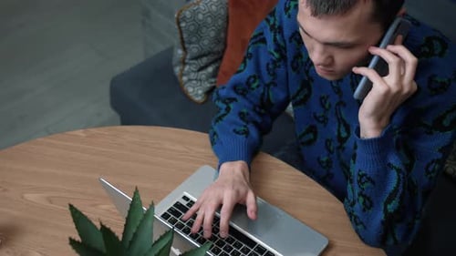 Close Up Caucasian Man Talking on the Phone While Working with a Laptop at Home. Slow Motion.