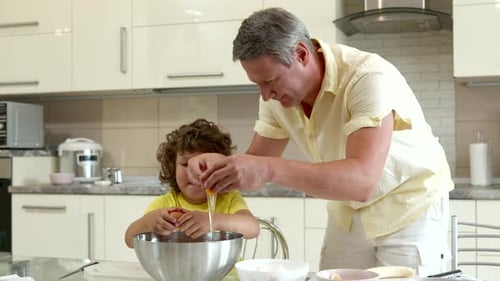Feliz padre y lindo hijo cocinan juntos rompiendo huevos en un tazón grande para masa