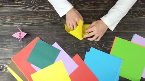 Hands Folding Origami on Desk With Colorful Papers