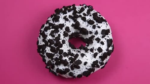 Iced Donut Topped with Crumbled Cookies on Pink Surface