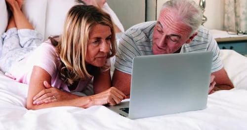 Mature Couple Using Laptop Together on White Bed