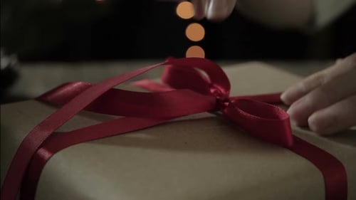Hands Tying Red Ribbon on a Christmas Gift