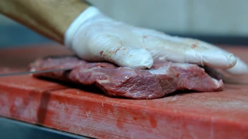 Gloved Hand Slicing Raw Red Meat on Cutting Board