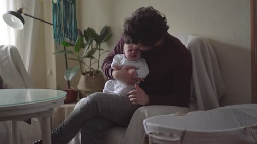 Dad embracing newborn baby in armchair at home