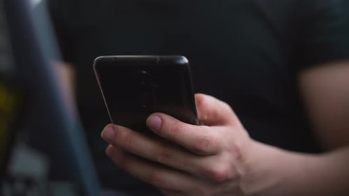 Person Scrolls News Feed on Mobile Phone Sitting at Laptop