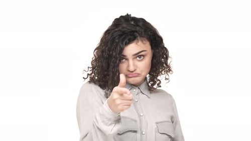 Porträt einer selbstbewussten, entschlossenen Frau, die den Zeigefinger vor der Kamera zeigt, was „Hey du“ über Weiß bedeutet