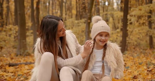 Woman Adjusting Hat on Smiling Girl in Autumn Woods