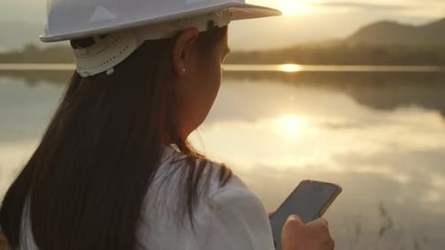 Female engineer working with a smartphone at the dam construction site to generate electricity.