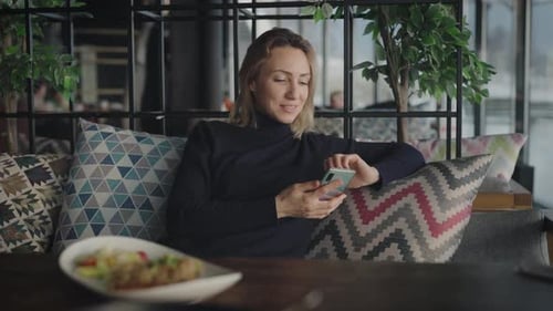 An Elegant Blonde in a Restaurant Uses a Smartphone