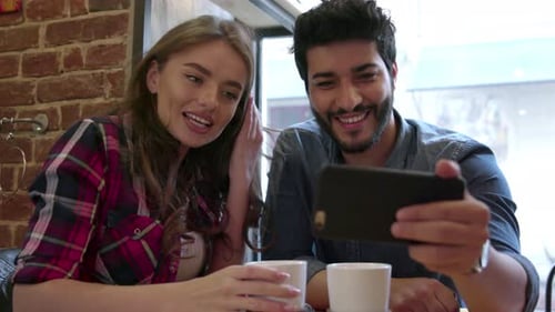 Video calling. Happy couple using phone for video call in cafe