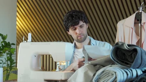 Young Adult Man Cutting Fabric at Sewing Machine